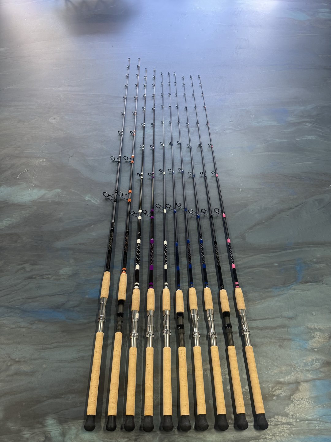 A set of ten rods fanned across the marbled work table, cork foregrips above black butt sections