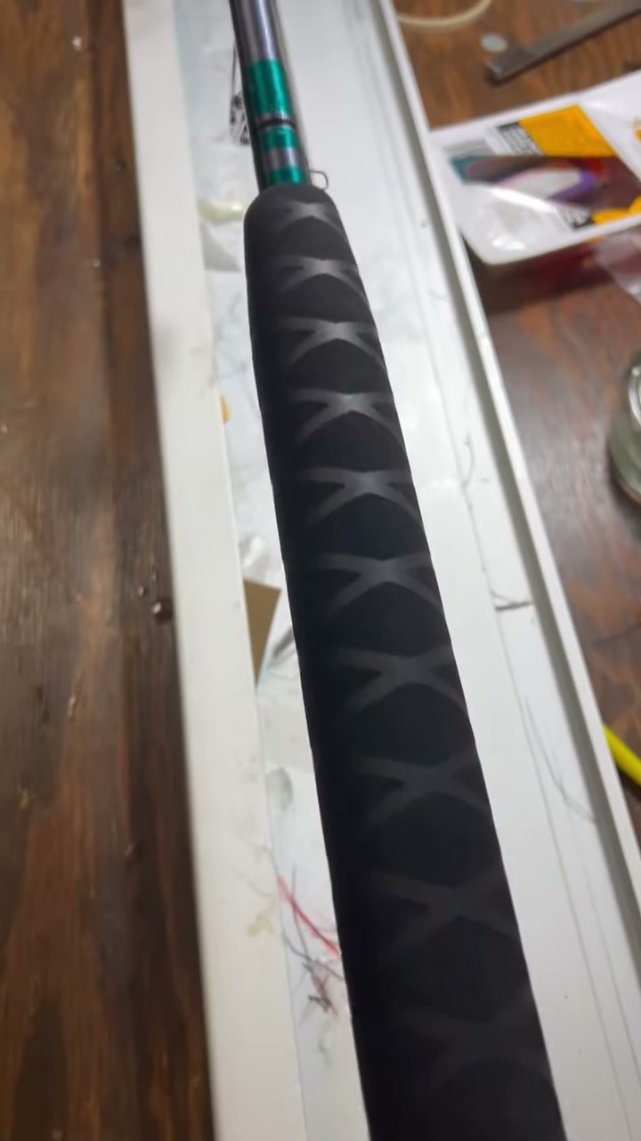 A black grip with a dark X-pattern wrap, resting on the shop bench