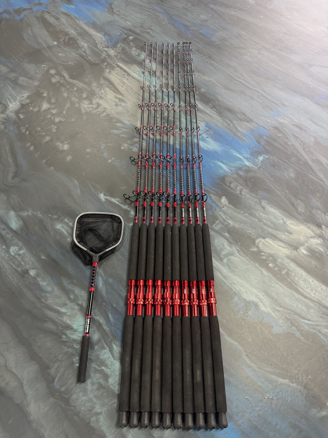 A set of rods wrapped in red thread laid out with a landing net on the marbled work table