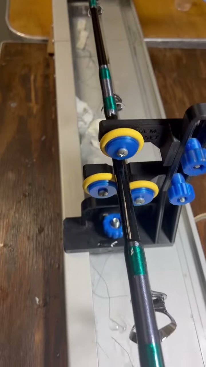 A rod blank sitting on the wrapping turner between its rollers, green thread laid down over the guide foot